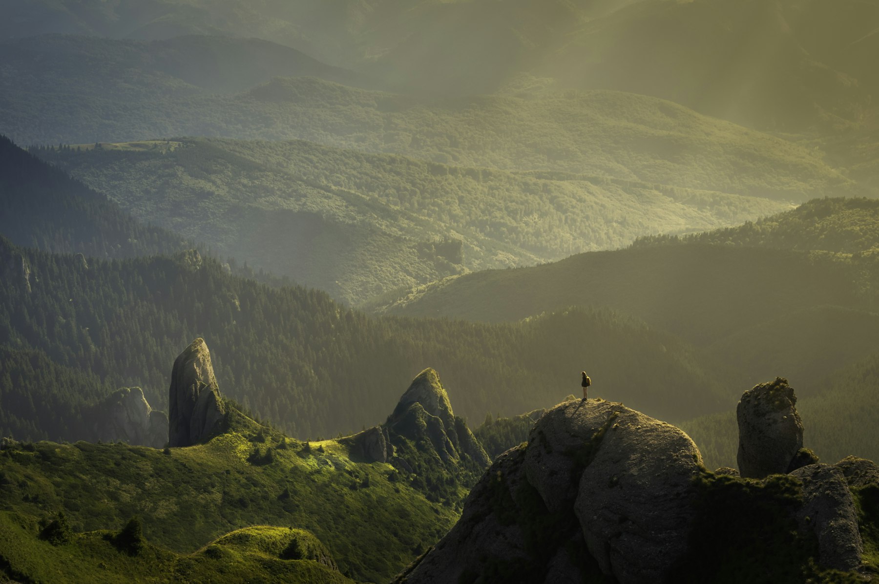 A person on a rocky ridge above misty valleys in warm light