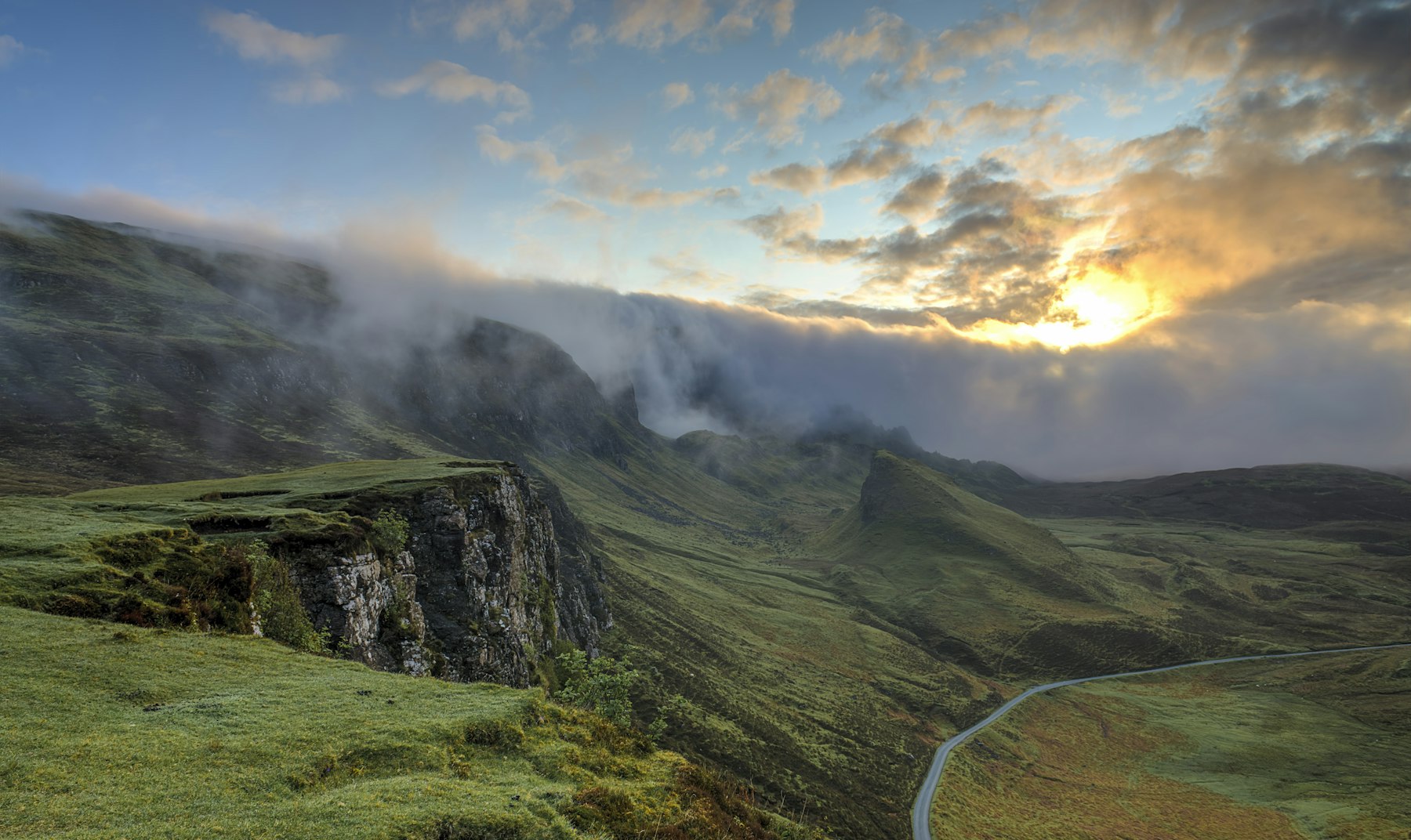 A winding road through green hills at sunrise